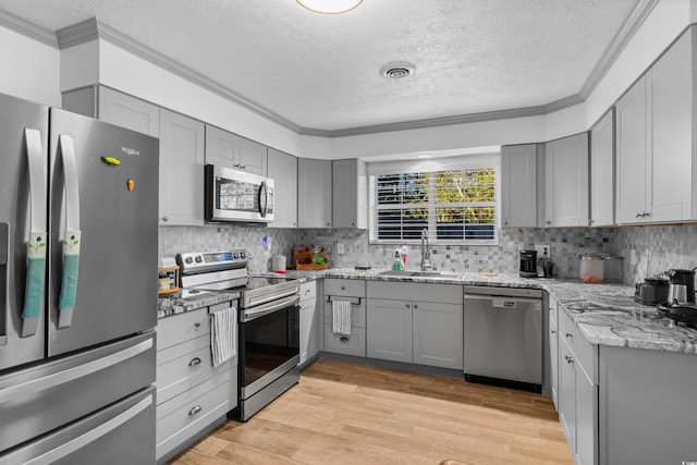 kitchen featuring sink, stainless steel appliances, light stone counters, ornamental molding, and light hardwood / wood-style flooring