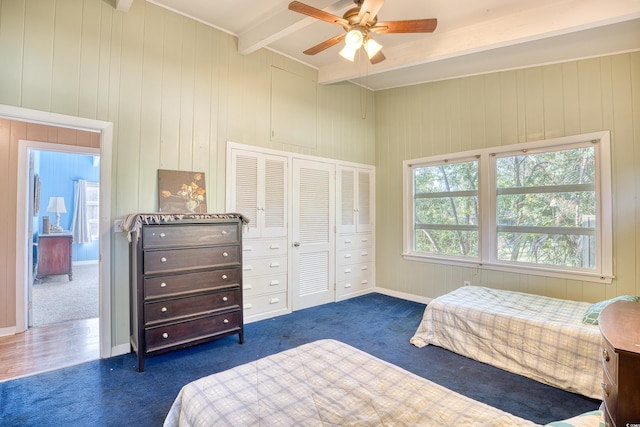 bedroom featuring beam ceiling, ceiling fan, dark carpet, a closet, and wooden walls