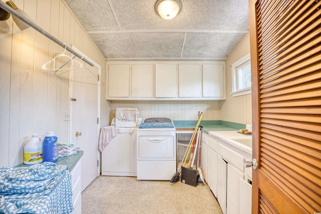 laundry room with wooden walls, light colored carpet, cabinets, washing machine and dryer, and a textured ceiling