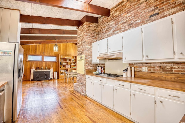 kitchen featuring beamed ceiling, light hardwood / wood-style flooring, stainless steel appliances, brick wall, and white cabinetry