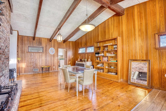 dining area with light hardwood / wood-style floors, wood walls, vaulted ceiling with beams, and plenty of natural light