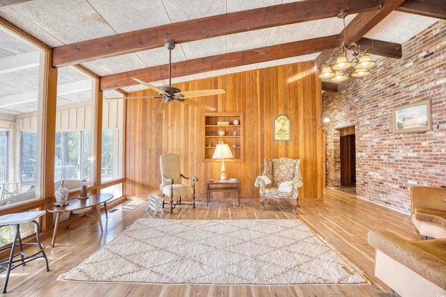 living area with hardwood / wood-style flooring, wooden walls, brick wall, and ceiling fan with notable chandelier