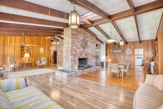 unfurnished living room featuring ceiling fan, hardwood / wood-style flooring, a brick fireplace, vaulted ceiling with skylight, and wooden walls