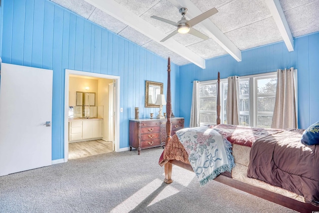 bedroom with connected bathroom, beam ceiling, ceiling fan, light wood-type flooring, and wood walls