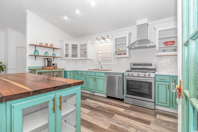 kitchen featuring butcher block counters, sink, stainless steel appliances, wall chimney range hood, and white cabinets