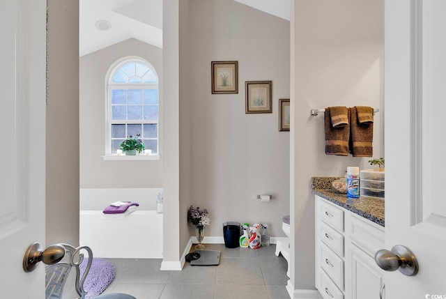 bathroom featuring vanity, lofted ceiling, tile patterned flooring, and a washtub