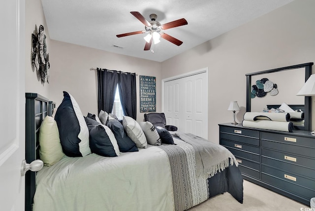 bedroom featuring a textured ceiling, light colored carpet, a closet, and ceiling fan