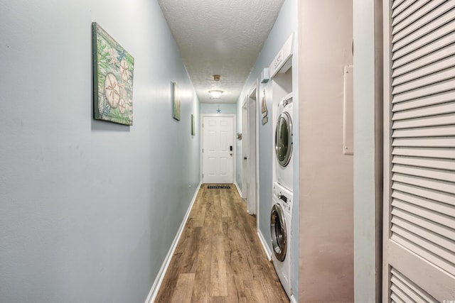 washroom featuring stacked washer and clothes dryer, a textured ceiling, and light hardwood / wood-style floors