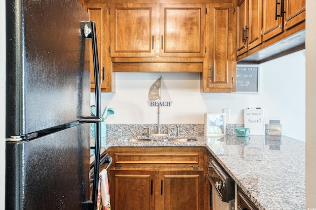 kitchen with black refrigerator, stainless steel dishwasher, and light stone counters