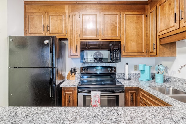 kitchen featuring light stone counters, sink, and black appliances