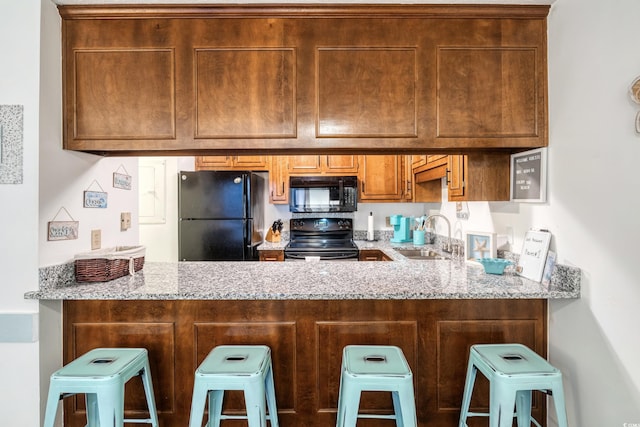 kitchen featuring light stone counters, a breakfast bar, sink, and black appliances