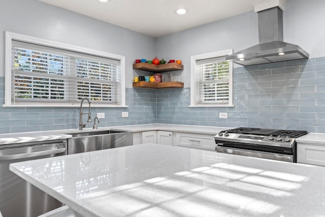 kitchen with wall chimney range hood, white cabinets, tasteful backsplash, sink, and stainless steel appliances