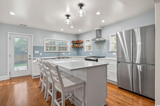 kitchen with wall chimney range hood, a center island, stainless steel appliances, and light hardwood / wood-style floors