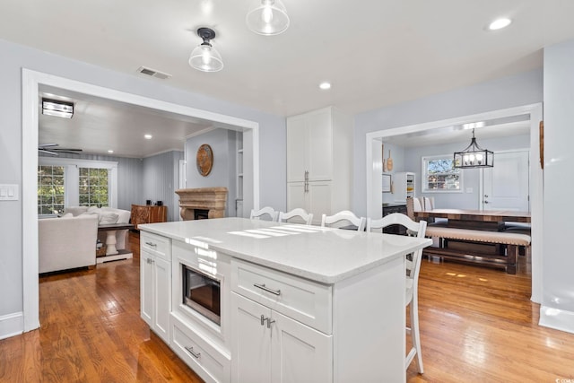 kitchen with stainless steel microwave, white cabinetry, decorative light fixtures, and a kitchen bar