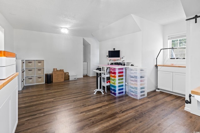 unfurnished office with lofted ceiling, a textured ceiling, a barn door, and dark hardwood / wood-style floors