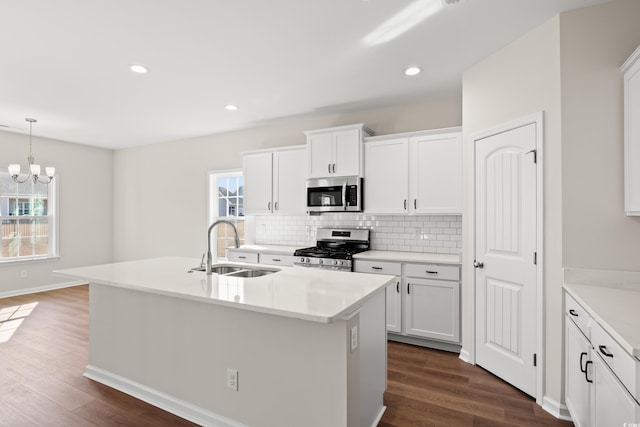 kitchen with white cabinetry, appliances with stainless steel finishes, a center island with sink, and hanging light fixtures