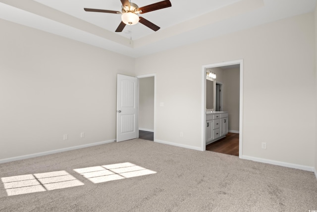 unfurnished bedroom featuring a raised ceiling, ceiling fan, connected bathroom, and dark colored carpet