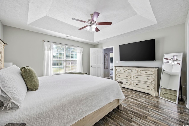 bedroom with dark wood-type flooring, ceiling fan, a textured ceiling, and a tray ceiling