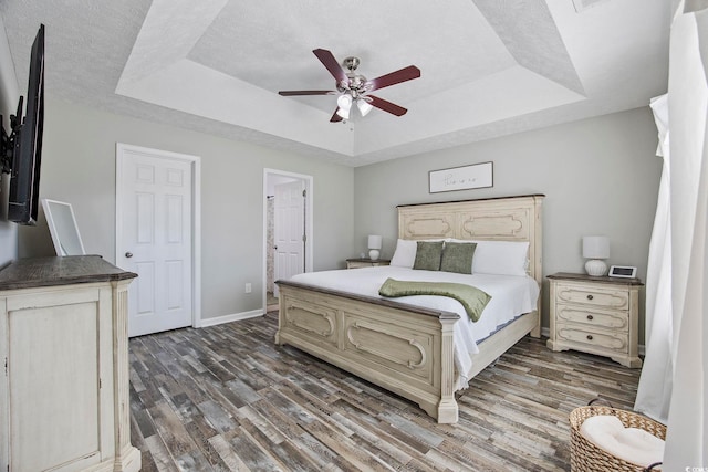 bedroom with dark hardwood / wood-style flooring, ensuite bath, ceiling fan, and a raised ceiling