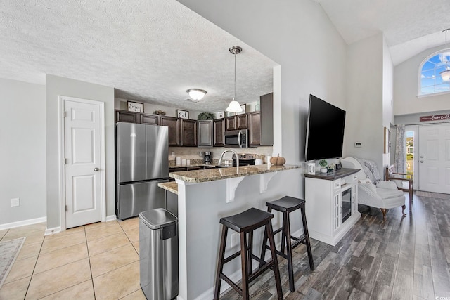 kitchen featuring dark brown cabinets, kitchen peninsula, light hardwood / wood-style floors, stainless steel appliances, and pendant lighting