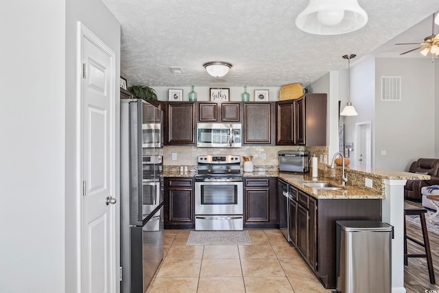 kitchen featuring kitchen peninsula, a kitchen bar, stainless steel appliances, sink, and decorative light fixtures