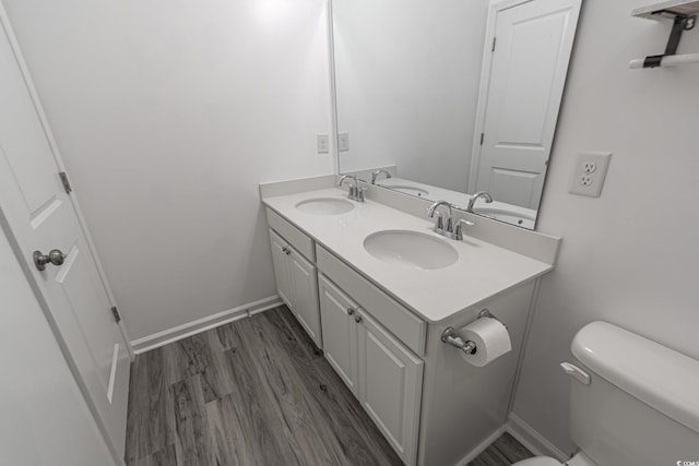 bathroom with double vanity, wood finished floors, a sink, and toilet