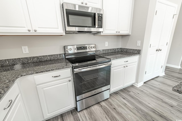 kitchen with appliances with stainless steel finishes, white cabinets, dark stone countertops, light wood-type flooring, and baseboards