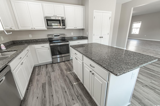 kitchen with appliances with stainless steel finishes, a center island, white cabinets, and wood finished floors