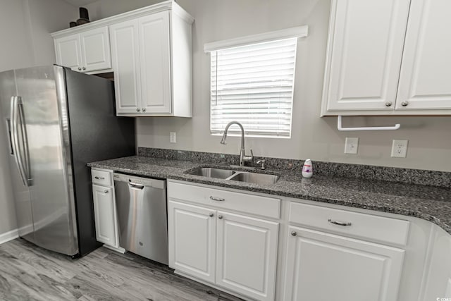 kitchen featuring light wood finished floors, appliances with stainless steel finishes, white cabinetry, a sink, and dark stone counters