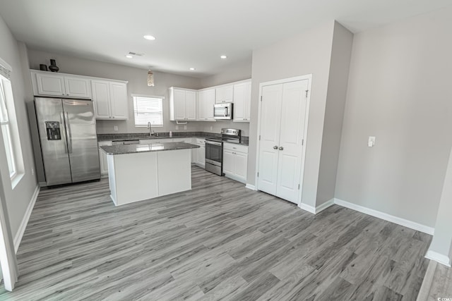 kitchen featuring dark countertops, a kitchen island, stainless steel appliances, white cabinetry, and a sink