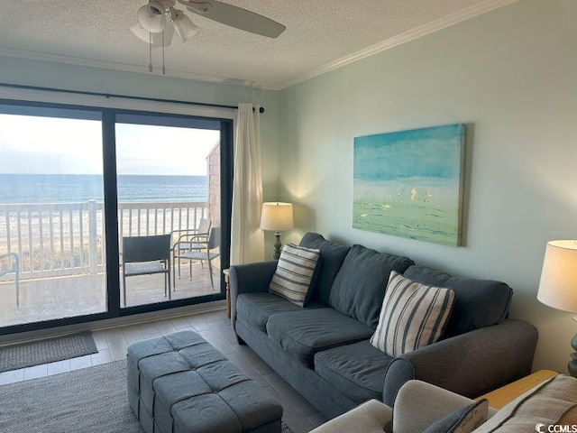 living room featuring a water view, a beach view, a textured ceiling, ornamental molding, and ceiling fan