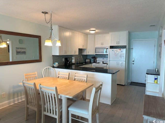 kitchen with kitchen peninsula, a textured ceiling, decorative light fixtures, white appliances, and white cabinets