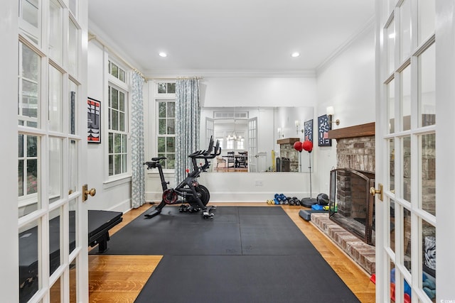 workout area with a brick fireplace, french doors, light hardwood / wood-style floors, and crown molding