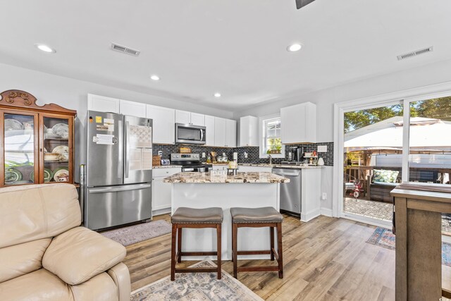 kitchen with tasteful backsplash, appliances with stainless steel finishes, a kitchen island, white cabinetry, and light hardwood / wood-style floors