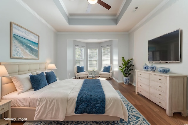 bedroom featuring a raised ceiling, ornamental molding, visible vents, and wood finished floors