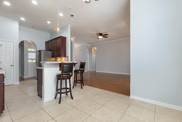 kitchen featuring a breakfast bar area, ornamental molding, ceiling fan, light tile patterned flooring, and decorative light fixtures