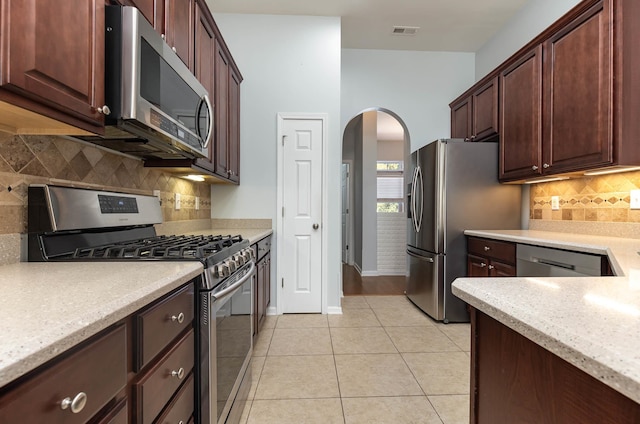 kitchen with stainless steel appliances, light stone counters, light tile patterned floors, and tasteful backsplash