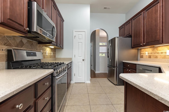 kitchen featuring stainless steel appliances, light tile patterned flooring, visible vents, backsplash, and arched walkways