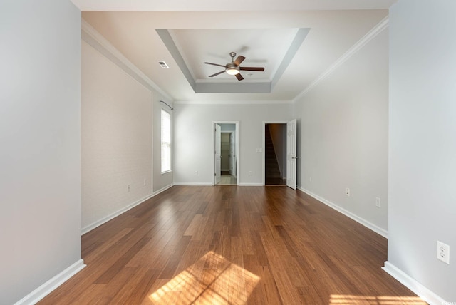 spare room featuring baseboards, ornamental molding, ceiling fan, wood finished floors, and a raised ceiling