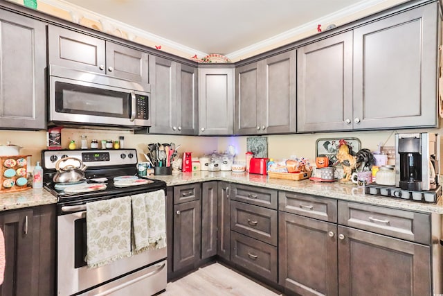 kitchen with appliances with stainless steel finishes, light hardwood / wood-style floors, light stone counters, and crown molding