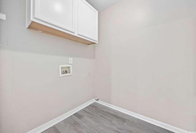 clothes washing area with hookup for a washing machine, cabinets, a textured ceiling, and light wood-type flooring