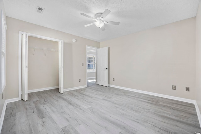 unfurnished bedroom with a textured ceiling, a closet, light hardwood / wood-style flooring, and ceiling fan