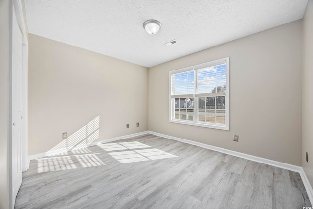 empty room with a textured ceiling and light hardwood / wood-style flooring