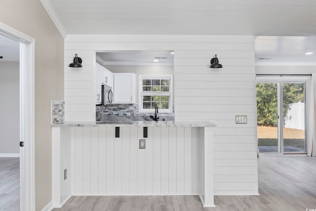 kitchen with white cabinets, light hardwood / wood-style floors, light stone counters, and wooden walls