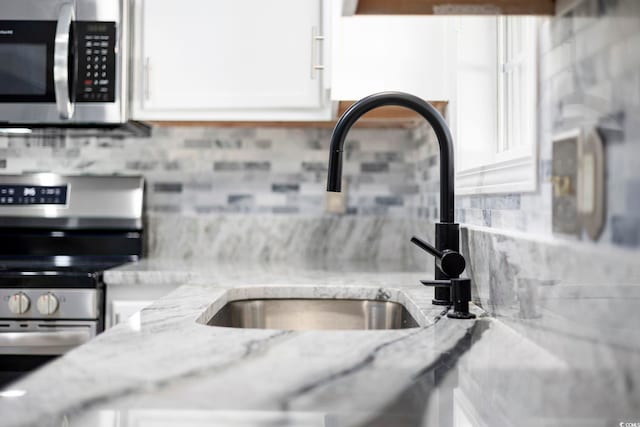 room details featuring sink, light stone counters, decorative backsplash, white cabinets, and appliances with stainless steel finishes