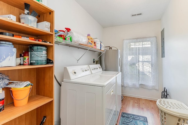 clothes washing area featuring water heater, light hardwood / wood-style flooring, electric panel, and washing machine and dryer