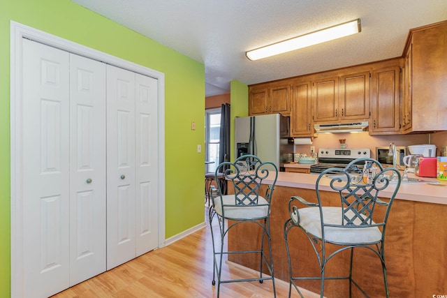 kitchen featuring appliances with stainless steel finishes, kitchen peninsula, a textured ceiling, and light wood-type flooring