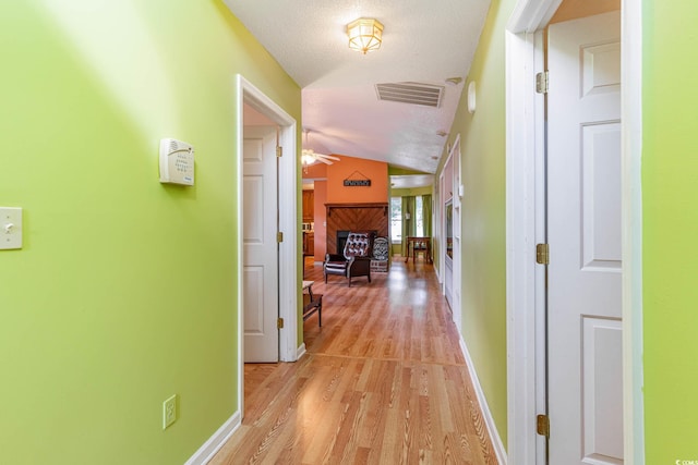 corridor with light hardwood / wood-style flooring, a textured ceiling, and vaulted ceiling