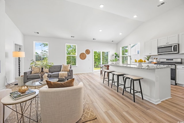 living area featuring light wood finished floors, visible vents, and high vaulted ceiling