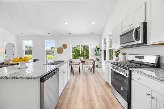 kitchen featuring light wood finished floors, stainless steel appliances, a sink, a center island with sink, and white cabinetry